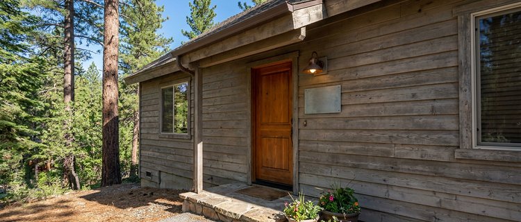 Wood-sided Big Bear rental cabin with a sign plaque beside the front door, where a licensed short-term rental posts its required contact and occupancy information